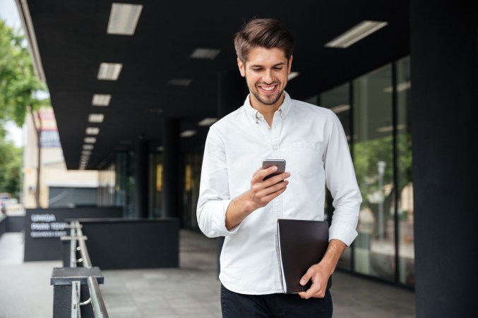 Happy businessman walking and using mobile phone outdoors